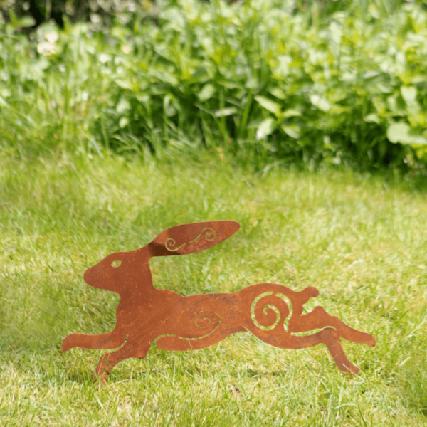 Running hare garden decoration made from rusted metal. Hare stands in the ground by stakes at the feet